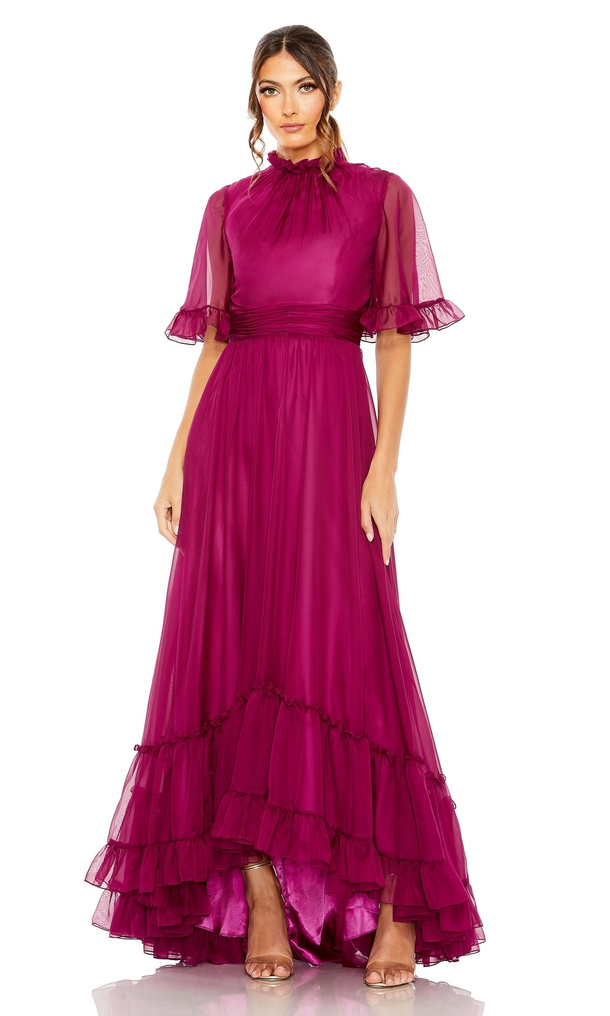 A woman wears the Mac Duggal 68229 short sleeve long formal dress in magenta, featuring ruffled sleeves and hem, a sheer overlay, and a fitted waist, paired with neutral heels.